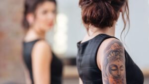 womensway 142 Egy nő hátán látható egy részletes Buddha-tetoválás, miközben egy másik nő háttal áll neki.