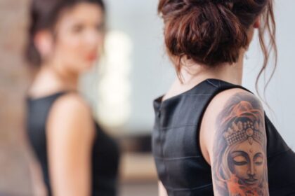 Egy nő hátán látható egy részletes Buddha-tetoválás, miközben egy másik nő háttal áll neki.