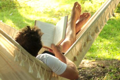 Egy férfi pihen a függőágyban, könyvet olvasva a zöld fűben.