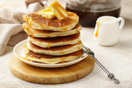 Egy tál amerikai palacsinta, vajjal és mézzel megöntözve, fából készült tányéron.