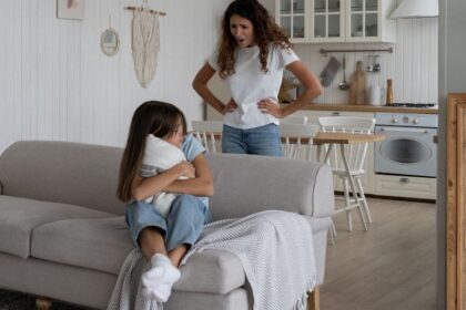 Egy kislány ül a kanapén, félelemmel az arcán, míg anyja dühösen néz rá.