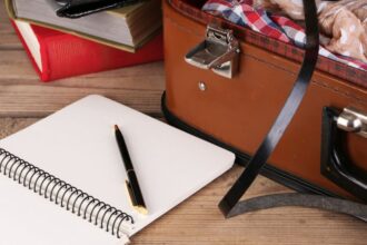 Egy nyitott bőrönd, mellette egy üres jegyzetfüzet és egy toll, utazási előkészületekhez.