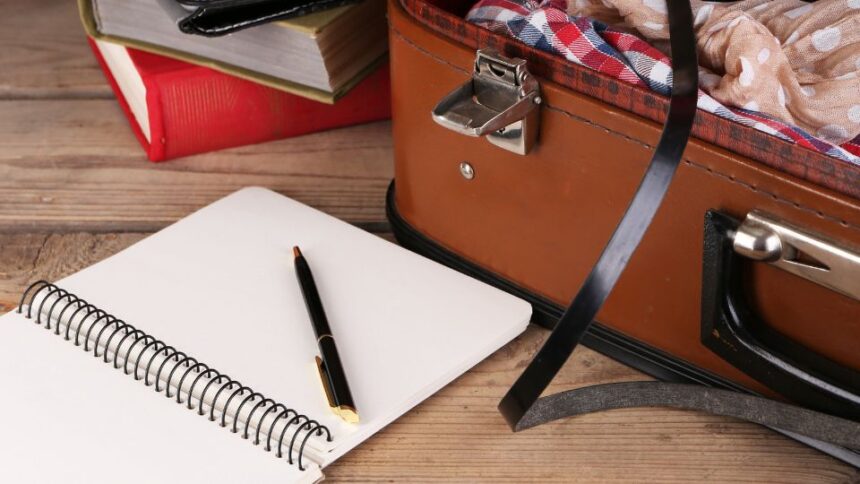 5 dolog, amit nem szabad elfelejteni utazás előtt 1 Egy nyitott bőrönd, mellette egy üres jegyzetfüzet és egy toll, utazási előkészületekhez.