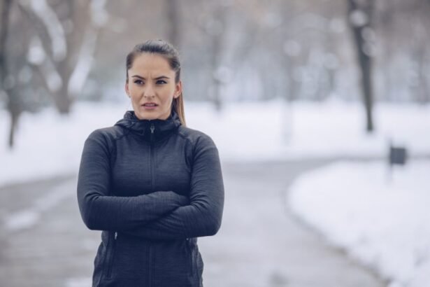 Egy nő sportos öltözetben áll a hóval borított parkban, karba tett kézzel, a hideg időjárás ellenére edzésre készül.