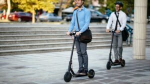 womensway 143 Két férfi elektromos rollerrel közlekedik egy városi téren, vidám hangulatban.