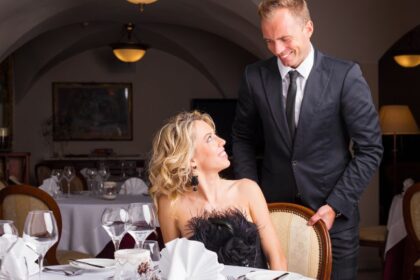 Egy elegáns étteremben egy férfi udvariasan segít egy nőnek az asztalnál, mindketten mosolyognak.