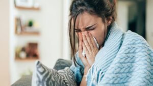 womensway 132 Egy fiatal nő, aki takaróba burkolózva, zsebkendőt használva küzd az influenzával.