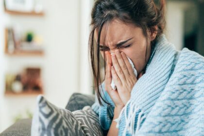 Egy fiatal nő, aki takaróba burkolózva, zsebkendőt használva küzd az influenzával.