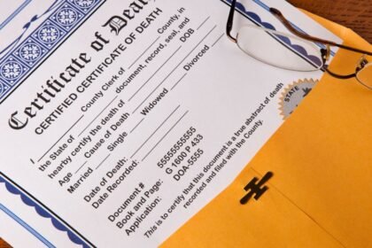 Egy halotti anyakönyvi kivonat, amelyen a fontos adatok láthatók, mellette egy szemüveg.