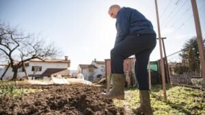 Egy férfi ásóval dolgozik a kertben, a napfényben, a talajforgatás érdekében.