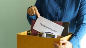 Egy kéz egy dobozban tartja a felmondólevelet, amely a munkahelyváltás szimbóluma.