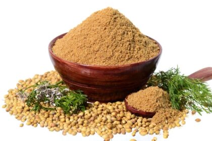 Egy tálban korianderpor, körülötte koriandermagok és friss fűszernövények.
