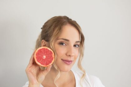 Egy fiatal nő mosolyogva tart a kezében egy fél grapefruitot, ami gazdag vitaminokban és antioxidánsokban, segítve az egészséges bőr fenntartását.