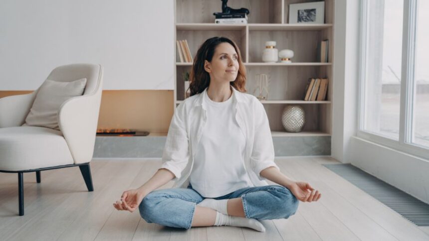 Egy nő meditál a világos, modern lakásban, nyugodt arckifejezéssel.
