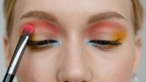 Egy nő színes szemsminket készít, rózsaszín, sárga és kék árnyalatokkal.