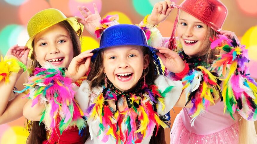Három vidám gyerek farsangi jelmezben, színes kalapokkal és tollakkal díszítve, boldogan mosolyognak.