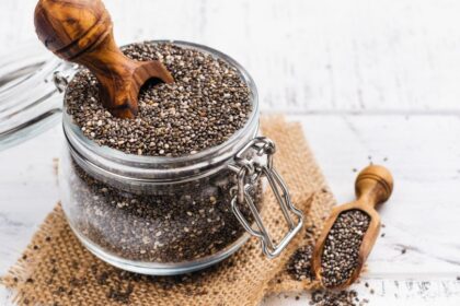 Egy üvegben chia magok láthatók, mellette egy kis fa kanál, amelyből néhány mag kiömlött.