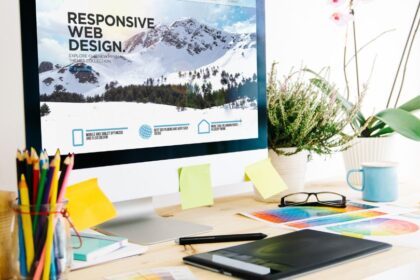 Egy modern munkahely grafikai tervezéshez, ahol egy számítógép képernyőjén responsive webdesign látható, színes ceruzák és tervezési anyagok mellett.