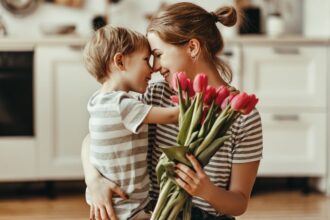 Egy édesanya és kisfia ölelkezik, miközben tulipánokat tart a kezében, a konyhában.