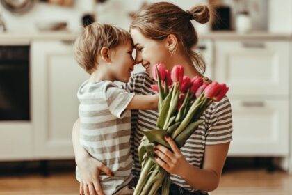 Egy édesanya és kisfia ölelkezik, miközben tulipánokat tart a kezében, a konyhában.