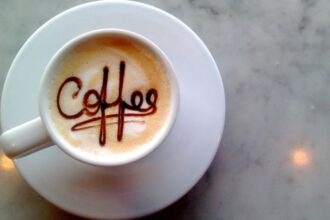 Egy csésze kávé, tetején a 'coffee' felirattal, fehér tányéron.