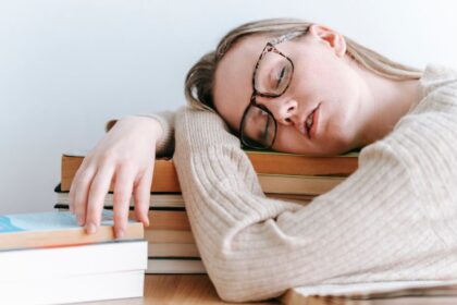 Fáradt fiatal nő könyvek között, az asztalon pihenve, kimerültség jeleit mutatja.