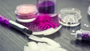 womensway 133 Műköröm készítéshez szükséges eszközök, mint a lakkok, csillámok és ecsetek egy asztalon.