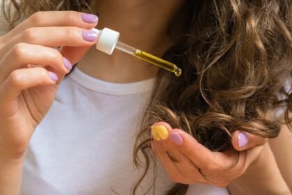 Egy nő kezében hajápoló olajjal teli pipetta, amelyet a göndör hajára csepegtet.