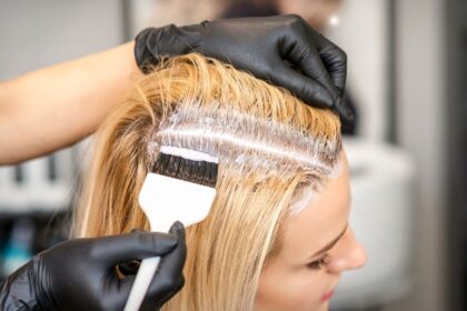 Egy nő haját festik otthon, fehér festéket visznek fel a gyökerekre.