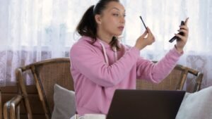 Egy fiatal nő sminket készít a tükör előtt, miközben otthon relaxál.