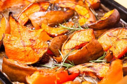 Sült tök szeletek rozmaringgal egy tepsiben, aranyló színben, ízletes és egészséges étel.