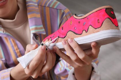 Egy fiatal nő színes, fánkos mintát fest egy vászoncipőre, kreatív textilfestési technikát alkalmazva.