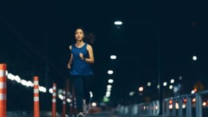 Egy fiatal nő fut az éjszakai utcán, világító lámpák alatt, biztonságos környezetben.