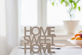 Egy világos, rendezett otthonban található 'HOME SWEET HOME' felirat, háttérben növényekkel.