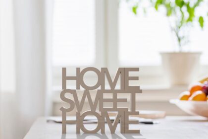 Egy világos, rendezett otthonban található 'HOME SWEET HOME' felirat, háttérben növényekkel.