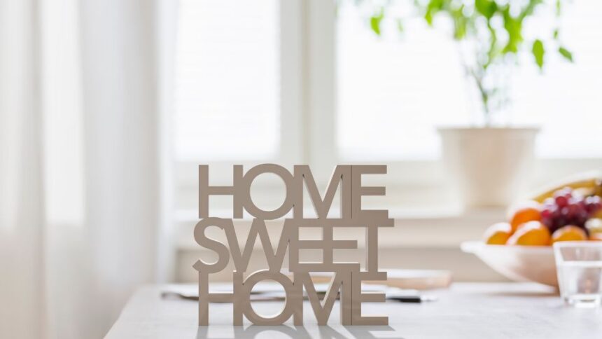 Egy világos, rendezett otthonban található 'HOME SWEET HOME' felirat, háttérben növényekkel.