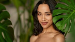 Egy fiatal nő mosolyog, háttérben zöld növényekkel, természetes szépséggel.