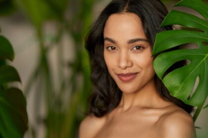 Egy fiatal nő mosolyog, háttérben zöld növényekkel, természetes szépséggel.