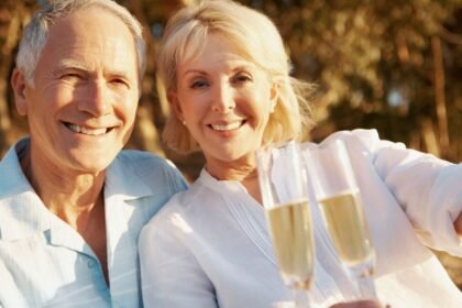 Egy idős pár boldogan mosolyog, miközben pezsgőt koccintanak a szabadban.