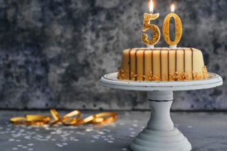 Egy díszes torta, amelyen aranyszínű 50-es gyertya áll, ünnepi hangulatot teremtve.