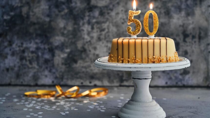 Egy díszes torta, amelyen aranyszínű 50-es gyertya áll, ünnepi hangulatot teremtve.