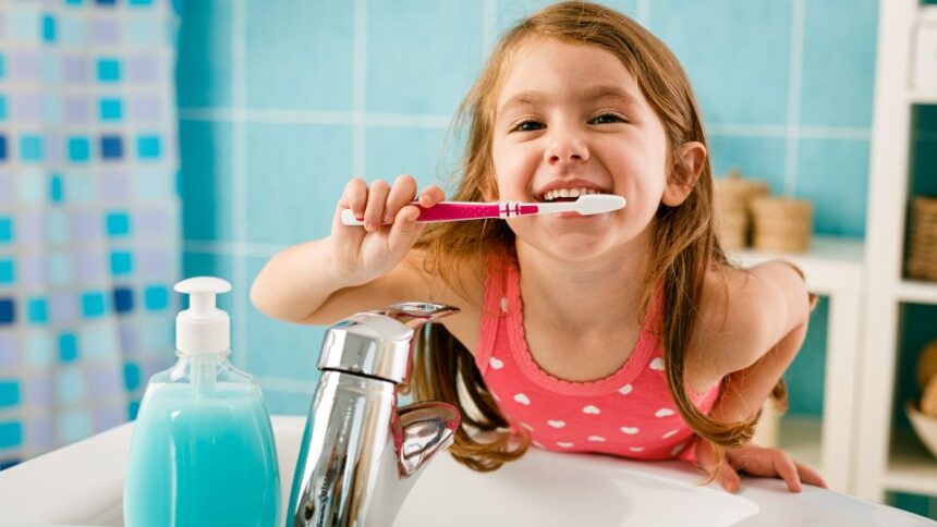 Hogyan szoktassam rá a gyereket a rendszeres fogmosásra? 1 Egy kisgyermek boldogan fogat mos a fürdőszobában, miközben a tükör előtt áll.