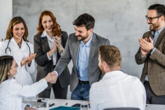 Egy új munkatárs üdvözlése a munkahelyen, ahol a csapat tagjai örömmel tapsolnak és gratulálnak.