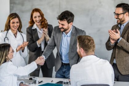 Egy új munkatárs üdvözlése a munkahelyen, ahol a csapat tagjai örömmel tapsolnak és gratulálnak.