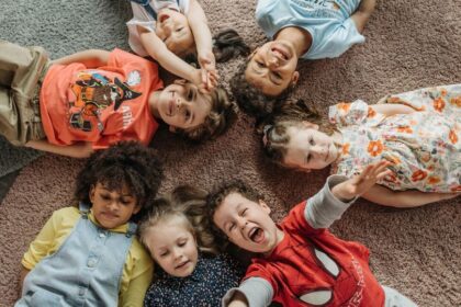 Hat kisgyermek fekszik a szőnyegen, vidáman mosolyogva, különböző ruhákban.