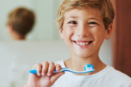Egy mosolygó kisfiú fogkefével a kezében, készülődik a fogmosásra.