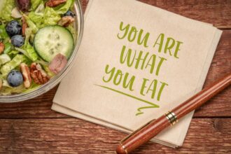 Friss saláta tál, tele zöldségekkel és gyümölcsökkel, mellett egy papíralátét, amelyen a 'You are what you eat' felirat olvasható.