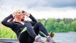 Két ember edz a szabadban, a nő hasizomgyakorlatot végez, miközben a természetben pihen.