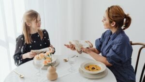 womensway 134 Két nő ül egy étkezőasztalnál, beszélgetnek és étkezési illemszabályokat tanulnak.