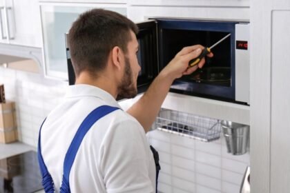 Egy férfi mikrohullámú sütőt javít, miközben csavarhúzót használ a belső alkatrészek ellenőrzéséhez.